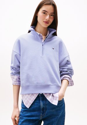 Lichtpaarse sweatshirt met hoge kraag en ritssluiting, gedragen over een geruit shirt. Katoenen stof met ribgebreide manchetten en zoom.