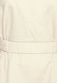 Vestido envolvente de creme claro com um tecido texturizado e amassado, apresentando uma cintura elástica para ajuste e um caimento lisonjeiro.