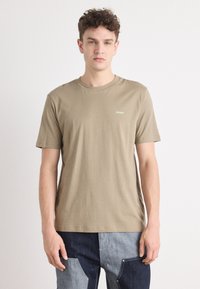 Khaki kortærmet T-shirt lavet af bomuld, med rund hals og lille grønt "HUGO" logo på venstre bryst. Blød tekstur.