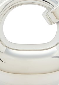 Kettle in argento lucido con corpo curvo, manico aperto e beccuccio largo. La superficie è liscia, con una finitura riflettente e dettagli di design minimi.
