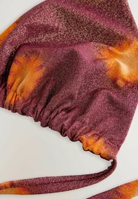 Violetti ja oranssi kuvioitu bikinitoppi, jossa on teksturoitu pinta. Sisältää rypytetyn kankaan ja säädettävät nauhat. Kiiltävä materiaali, jossa on hieno kimalle.