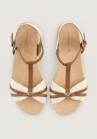 Braune und beige Sandalen mit einem T-Bar-Design, weichen Texturriemen und einem metallischen Akzentdetail. Flache Sohle mit gepolstertem Fußbett.