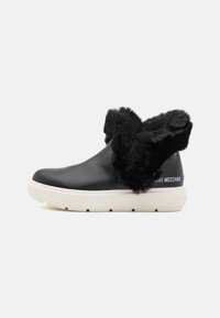 Svarta läderankelstövlar med en krage av konstig päls, vit gummisula och präglad logotyp på hälen. Slät textur med mjuka detaljer.