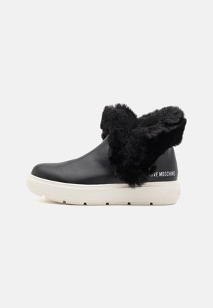 Black leather ankle boot with a faux fur collar, white rubber sole, and embossed branding on the heel. Smooth texture with plush accents.