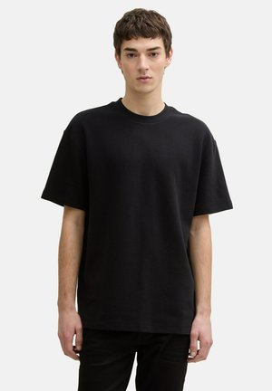 Zwarte textuur t-shirt met een ronde halslijn en korte mouwen, getoond op een persoon tegen een effen, lichte achtergrond.