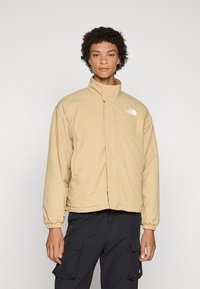 Beež, lukuga jope kõrge kraega ja elastsetega varrukatega, millel on North Face'i logo. Sile tekstuur, kerge disain, lõdvestunud sobivus.