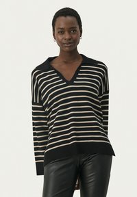 Zwart en beige gestreepte trui met een v-hals, lange mouwen en een kraag. Zachte textuur en een comfortabele pasvorm, gecombineerd met zwarte leren broeken.