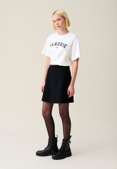 Camiseta blanca con "CLAUDIE PARIS" impreso en negro, combinada con una falda negra acampanada y botas de tobillo negras con cordones.