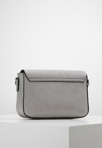 Šedá syntetická crossbody taška s klopou, černými detaily a stříbrným kováním na boční straně. Hladký povrch, obdélníkový tvar.