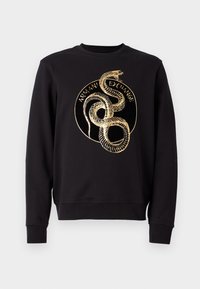 Svart långärmad sweatshirt med guldspiralformat ormgrafik och texten "Armani Exchange" i cirkulär design på framsidan.