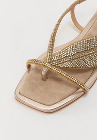 Infradito metallici dorati con dettagli in strass, plantare morbido beige, forma della punta quadrata e sottili fasce con design incrociato.