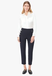 Blouse en satin blanc avec deux poches et manches longues, associée à un pantalon tailleur bleu marine avec des accents de boutons et une silhouette ajustée.