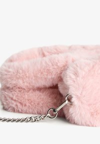 Lažna krznena okrugla torba u mekoj ružičastoj boji s teksturiranom površinom. Ima srebrni lanac za nošenje i kopču za sigurno zatvaranje.