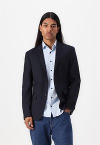 Navy blazer with notched lapels, single-button closure, and two front pockets, over a light blue shirt featuring dark buttons and long sleeves.