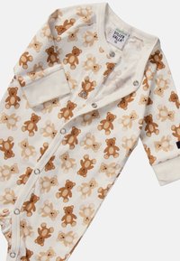 Tutina per neonato realizzata in morbido cotone biologico, con una base crema decorata da un motivo di orsetti di cartone nei toni del marrone. Chiusure a scatto.
