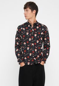 Chemise noire à manches longues ornée d'un motif de fête avec des Pères Noël, des flocons de neige et des cannes en sucre. Fabriquée en tissu léger.