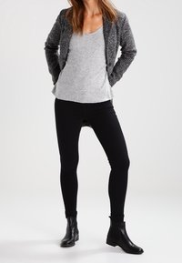 Blazer grigio a maglia sopra un top grigio, jeans skinny neri e stivali neri alla caviglia. Il blazer ha un motivo testurizzato e una vestibilità su misura.
