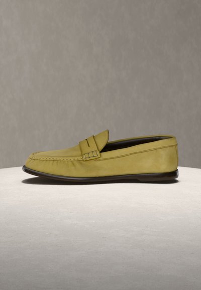 Mocassin en cuir jaune avec bride à monnaie, semelle plate foncée et couture visible sur l\'avant, présenté sur une surface claire avec un fond uni.