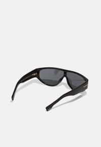 Occhiali da sole neri con un design elegante, lenti scure, montatura curva e sottili rifiniture dorate sulle aste. Presentano una forma moderna e angolare.