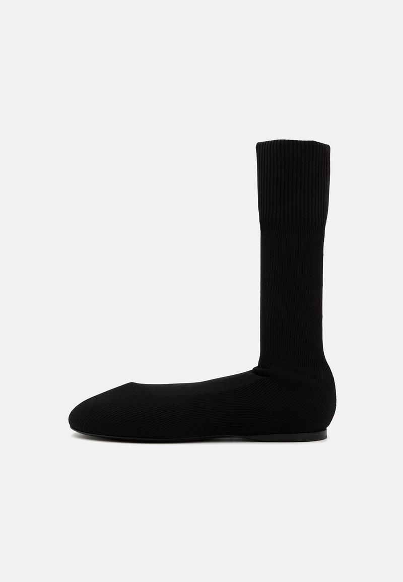 Ciorap negru tricotat până la gleznă, cu design ribat, formă închisă la vârf, textură netedă, cu o talpă din cauciuc plat pentru aderență.