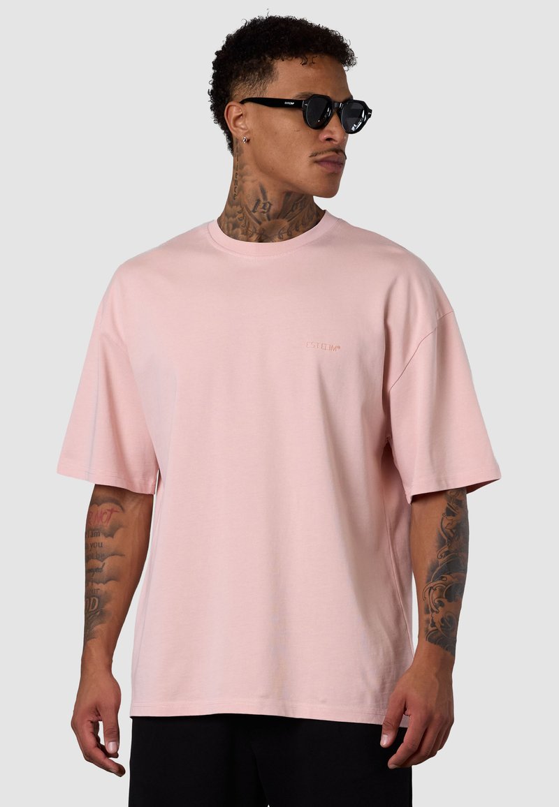 Light pink oversized t-shirt made of cotton. Short sleeves, crew neck, and subtle logo print on the chest. Smooth texture.