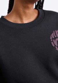 Sweat-shirt noir à col rond, avec un motif graphique violet sur la poitrine. Le tissu semble lisse avec une texture douce.