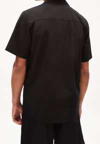 Czarna koszula z krótkim rękawem o luźnym kroju, wykonana z gładkiej tkaniny, z klasycznym kołnierzykiem typu point. Minimalistyczny design, bez widocznych wzorów.