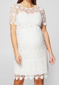 Vitt spetsklänning med korta ärmar, blommönster, figursydd bodice och resårmidja. Innehåller detaljer med vågkantade fållar. Midilängd.