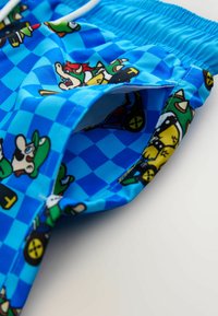 Bañador azul con un patrón a cuadros que presenta personajes de dibujos animados. Hecho de tela ligera con una cintura elástica y cordón ajustable.