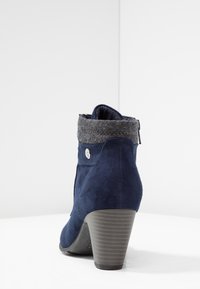 Donkerblauwe suède enkellaars met een grijze vilten kraag, geribbelde grijze hak, ritssluiting en een klein metalen accent aan de zijkant. Getextureerd oppervlak.