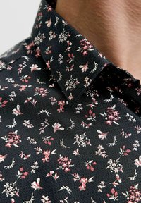 Koszula w kwiatowy wzór na czarnym tle; posiada małe różowe i białe kwiaty; ma zakładany kołnierzyk i teksturowany materiał.