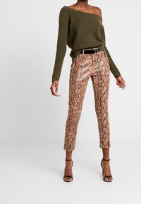 Off-the-shoulder olive green ribbed sweater paired with fitted snake-print trousers in shades of brown and black, featuring a belted waist.