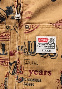 Bežna tkanina Levi's s vintage uzorkom, rajsferšlusima i brončanim detaljima. Na oznaci piše "AUTENTIČNA OBUĆA ZA ZAPAD" i "PIXAR."