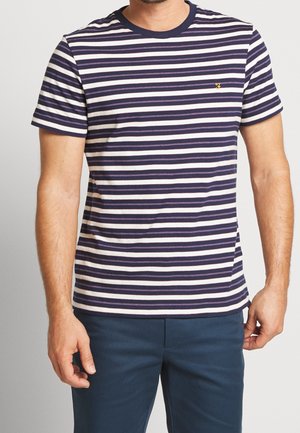 Hombre con una camiseta de manga corta de rayas horizontales azul marino y blanca con un pequeño logo amarillo en el pecho, combinado con pantalones azul oscuro.