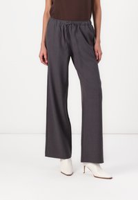 Pantalons gris à jambes larges avec une taille élastique, présentant une texture lisse et une apparence ajustée, associés à des bottes à talons blanches.