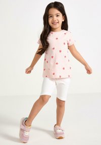 Vaaleanpunainen lyhythihainen t-paita, jossa on pieniä punaisia mansikkakuviota, yhdistettynä valkoisiin shortseihin ja vaaleanpunaisiin tennareihin, joissa on tarranauhat.