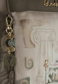 Graue Lederhandtasche mit einem dekorativen Design aus Säulenumrissen und Wirbeln. Enthält goldene Beschläge und Schmuckanhänger.