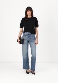 Schwarzes Kurzarmoberteil, hochtaillierte hellblaue Jeans, weit geschnitten, leicht ausgefranster Saum und schwarze Handtasche mit silbernem Zubehör.