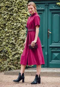 Burgundy dress with short sleeves, belted waist, and knee-high slit, paired with black block-heel ankle boots and a dark wallet. Green door背景.