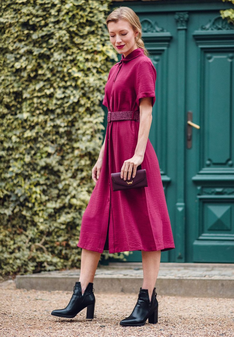 Burgundy dress with short sleeves, belted waist, and knee-high slit, paired with black block-heel ankle boots and a dark wallet. Green door背景.