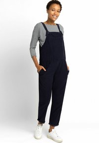 Marineblauwe corduroy-broeksalons met een losse pasvorm, verstelbare bandjes, een voorzak en zijzakken, gecombineerd met een gestreept shirt met lange mouwen en witte sneakers.