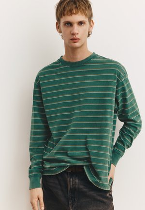 Maglietta verde a maniche lunghe con strisce orizzontali bianche e marrone chiaro. Scollo rotondo, vestibilità ampia, texture morbida e polsini a costine.