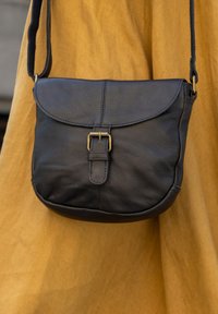 Sort læder crossbody taske med en buet klap, spændehardware og en tekstureret overflade. Remmen er justerbar, og formen er rund.