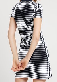 Polo dress w paski z granatowym kołnierzykiem, krótkimi rękawami i dopasowanym kształtem, lekko rozszerzanym u dołu oraz z bocznymi rozcięciami.
