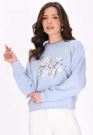 Helles blaues Sweatshirt mit langen Ärmeln und gerippten Bündchen, mit dem Aufdruck "Shine Bright" in goldfarbener Folienbeschriftung auf der Vorderseite.