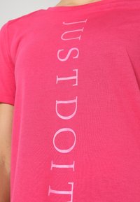 Rosa bomullströja med vertikal vit text som säger "JUST DO IT." Har rund halsringning och korta ärmar.