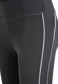 High-waisted black leggings with white side stripes, made from stretchy fabric, featuring flat seams and a smooth, matte texture.