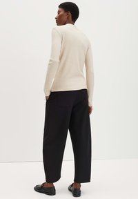 Helles beige Langarmoberteil mit figurbetontem Schnitt, kombiniert mit lockeren schwarzen Hosen. Das Outfit zeichnet sich durch einen einfachen, klaren Look und eine angenehme Textur aus.
