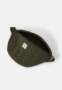 Olivgrüne gesteppte Schultertasche mit Reißverschluss, ausgestattet mit einem kleinen Logopatch und einem Stoffgurt zum Tragen.