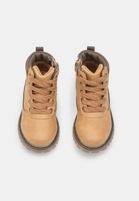 Stivali alla caviglia in pelle cuoio con colletto imbottito marrone, dotati di lacci tondi, cerniere laterali e suole in gomma testurizzata.